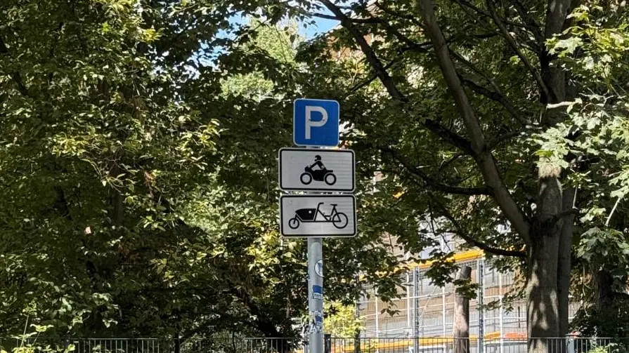 A blue P sign in Berlin with two plates under it, one showing a motorcycle and one showing a cargo bike, marking a bay both may use.