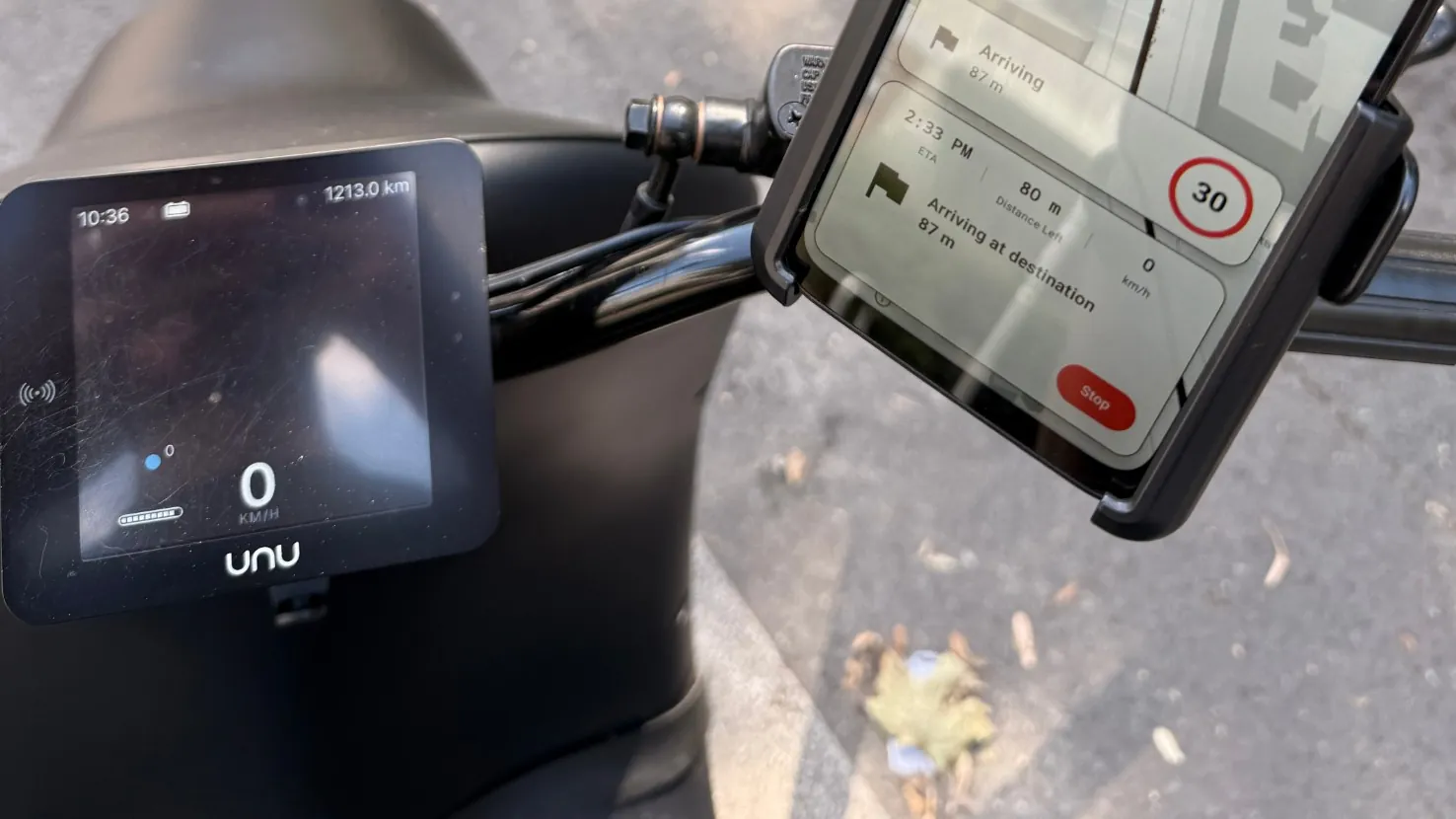 Een telefoon in een stuurhouder op een elektrische scooter, met de navigatie van Urban Rider in beeld: de afstand tot de volgende afslag en een maximumsnelheid van 30.